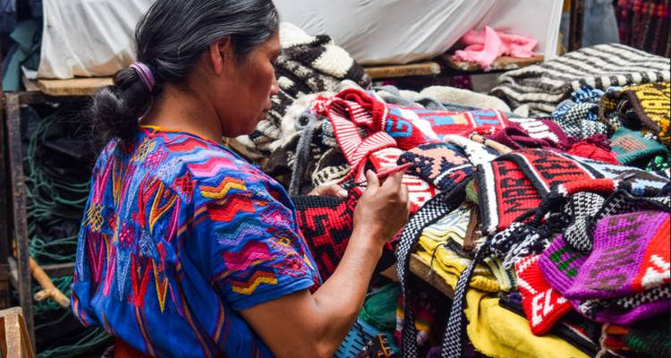 Femme en tenue traditionnelle tissant des textiles colorés au marché.