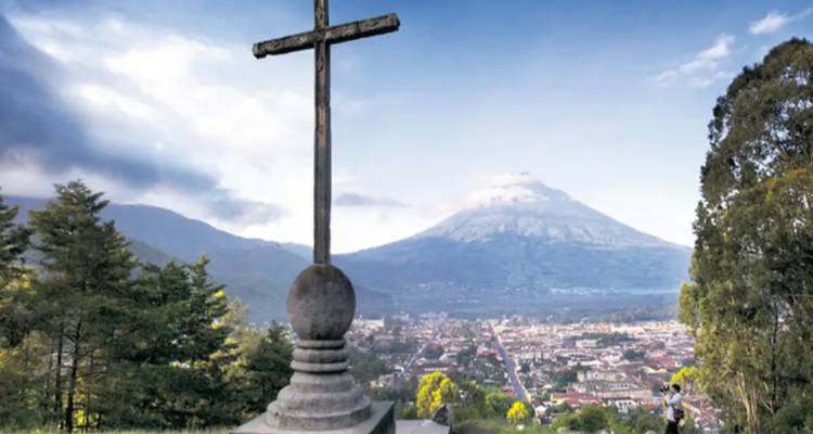 Vue sur la ville avec une croix proéminente et un volcan en arrière-plan.