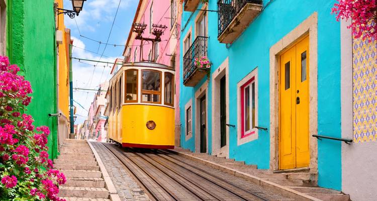 Un tramway jaune classique gravit une rue pavée escarpée bordée de bâtiments aux couleurs vives rose et turquoise et de bougainvilliers en fleurs à Lisbonne.