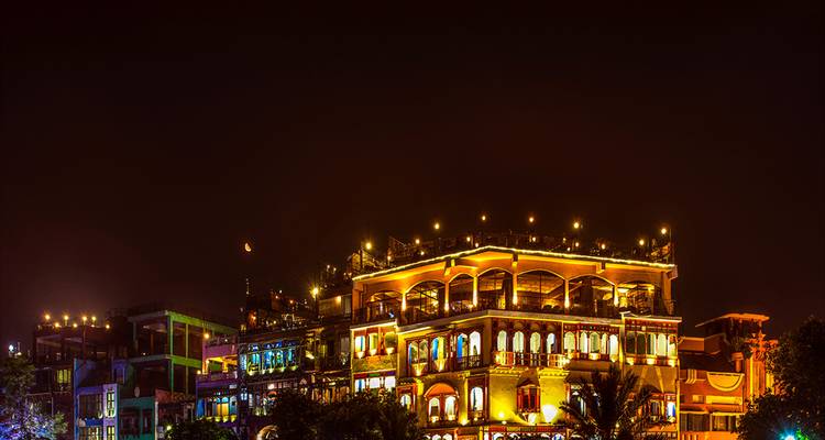 Rue alimentaire nocturne animée avec bâtiments patrimoniaux illuminés et lumières festives chaleureuses contre un ciel sombre