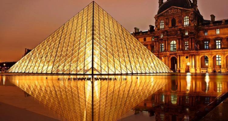 La Pyramide du Louvre illuminée la nuit avec son reflet dans l'eau.