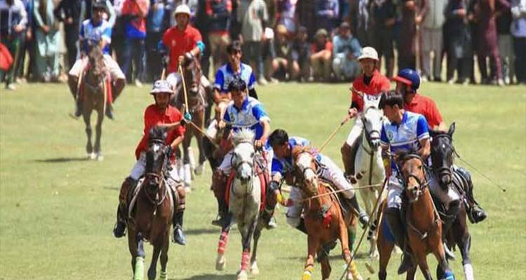 Match de polo rapide à Shandur sur un terrain herbeux avec des cavaliers en maillots colorés.