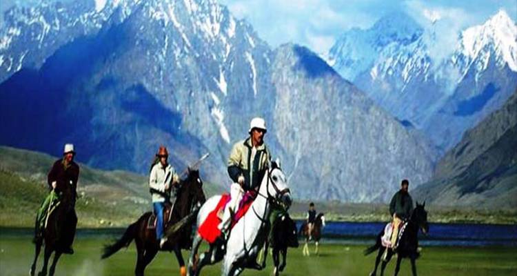 Les joueurs de polo à cheval galopent à travers une prairie avec en arrière-plan des montagnes enneigées spectaculaires et un lac.
