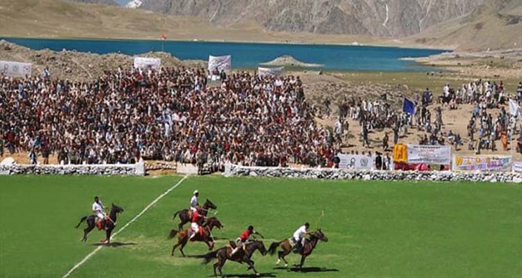 Une grande foule regarde un match de polo en altitude au bord d'un lac turquoise éclatant et de collines arides.