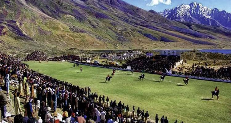 Vue large d'un terrain de polo herbeux entouré d'une grande foule et d'un paysage montagneux spectaculaire pendant un match de polo à cheval.