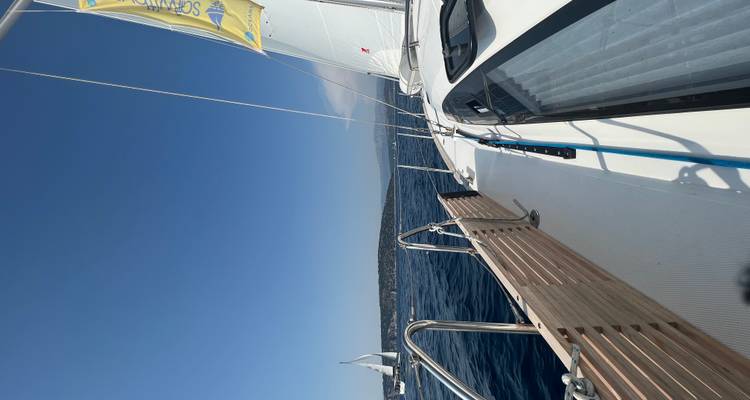 Een zeilboot op zee met ver land zichtbaar, vastgelegd vanaf het dek.