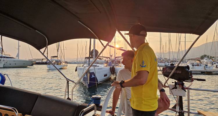 Mensen op een boot tijdens zonsondergang met jachthaven zichtbaar op de achtergrond.