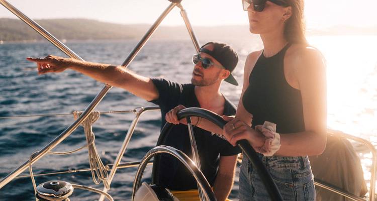 Pareja joven manejando un velero y señalando hacia el horizonte durante la luz dorada.