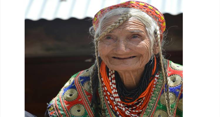 Anciana kalash sonriente con atuendo vibrante de cuentas y cabello trenzado.