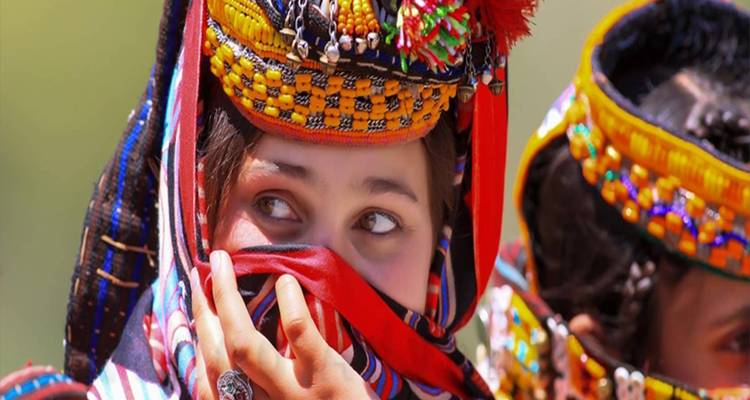 Joven niña Kalash se asoma juguetonamente desde detrás de un tocado colorido con cuentas.