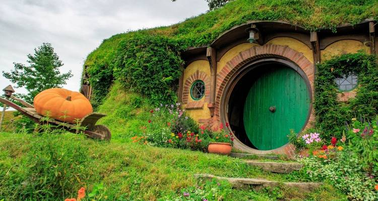 Maison de type hobbit avec une porte ronde située dans un paysage luxuriant.