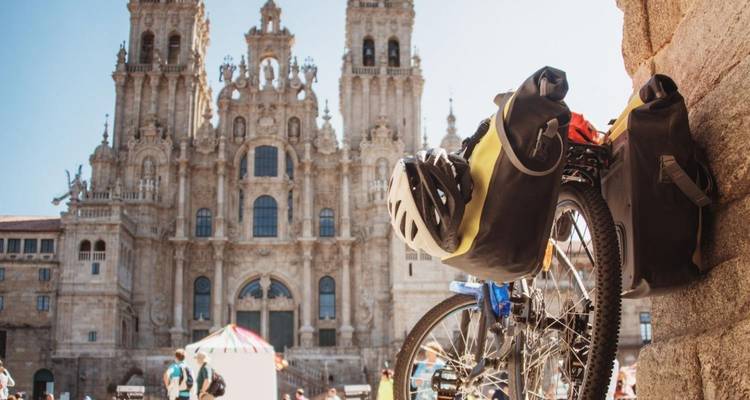 Beladen toerfiets leunend tegen een stenen muur met de kathedraal van Santiago de Compostela in zachte focus op de achtergrond