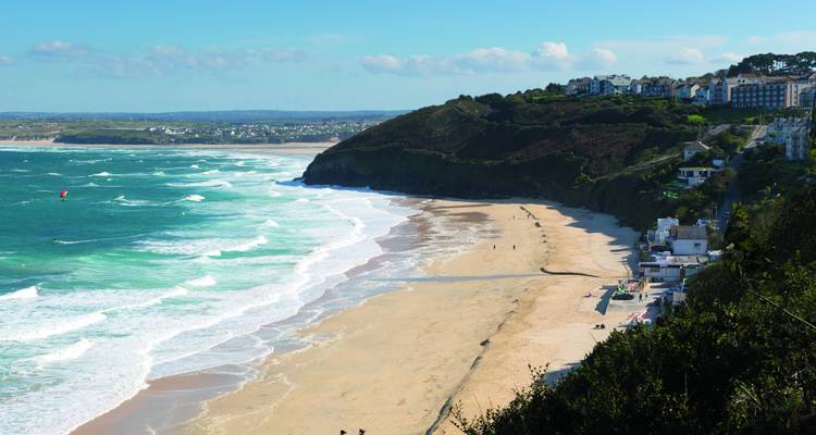 Sandstrand mit Wellen, Klippen und Gebäuden an der Küste.