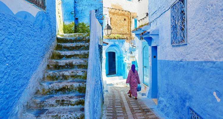 Smalle blauw gewassen steeg van Chefchaouen met een eenzame vrouw in gewaad die wegloopt.