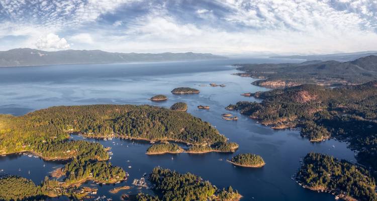 Panorama aéreo de islas costeras boscosas dispersas en un mar azul profundo bajo nubes con patrones.
