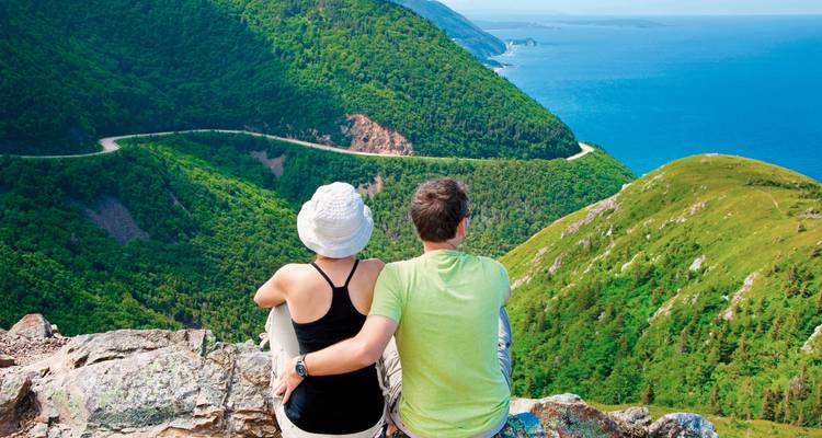 Paar sitzt auf einem Felsen mit Blick auf Berg und Meer.