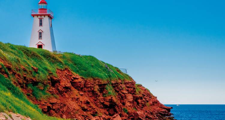 Leuchtturm auf einer grasbewachsenen Klippe am Meer.