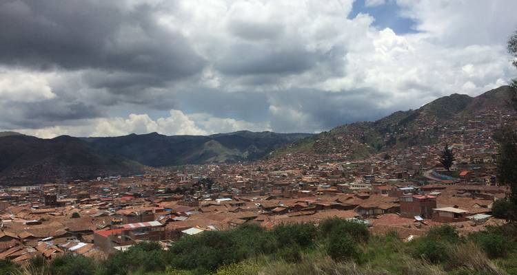 Panoramic view of a city with hills in the background under a cloudy sky.