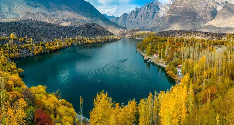 Panoramisch herfstlandschap van een diepblauw alpenmeer omringd door gele populieren en ruige bergen