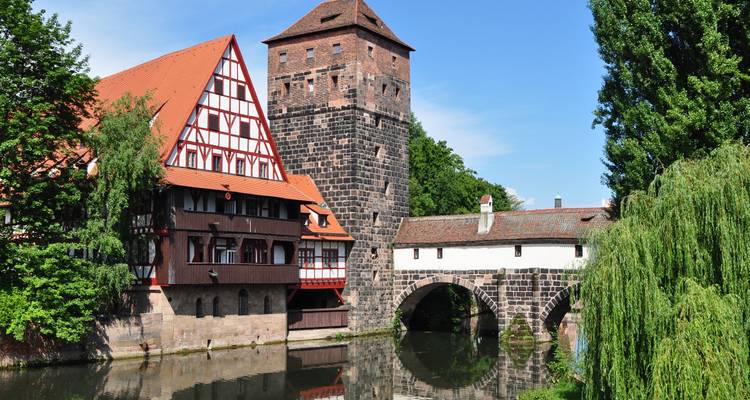 Old medieval buildings by the river with a pedestrian bridge.