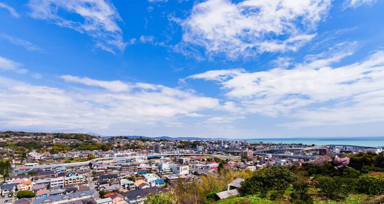 Sonnige Panoramablick über eine japanische Küstenstadt mit Autobahnen und Meereshorizont.