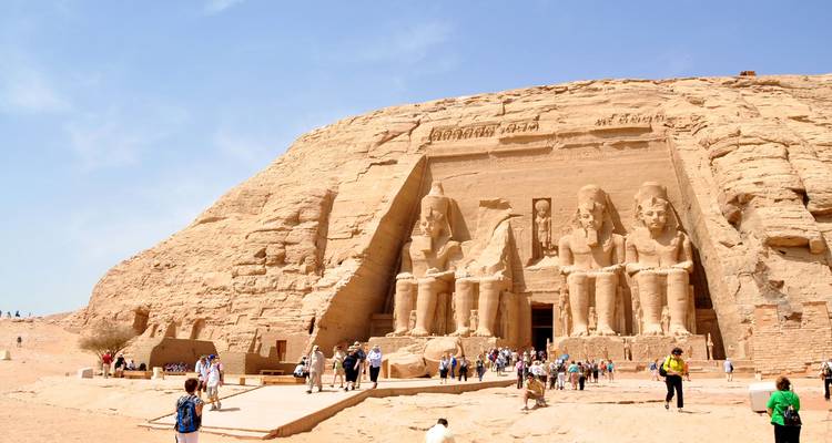 Statues assises massives de Ramsès II à Abou Simbel avec des touristes explorant la cour d'entrée du temple.