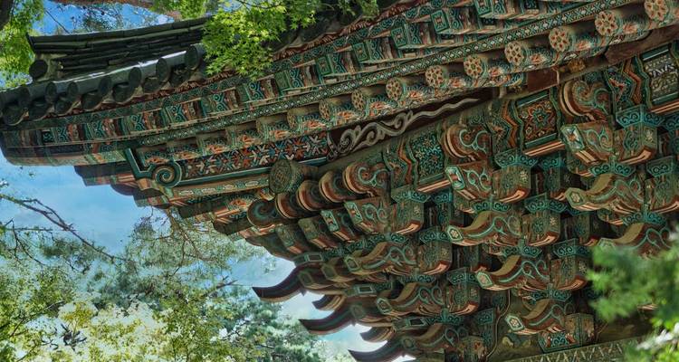 Ornately painted eaves of a traditional Korean building set against trees.