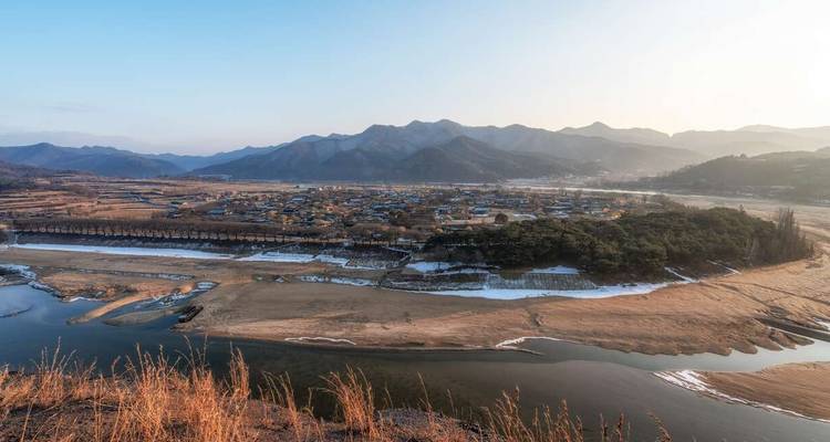 A panoramic view of a traditional Korean village with a river and mountains.