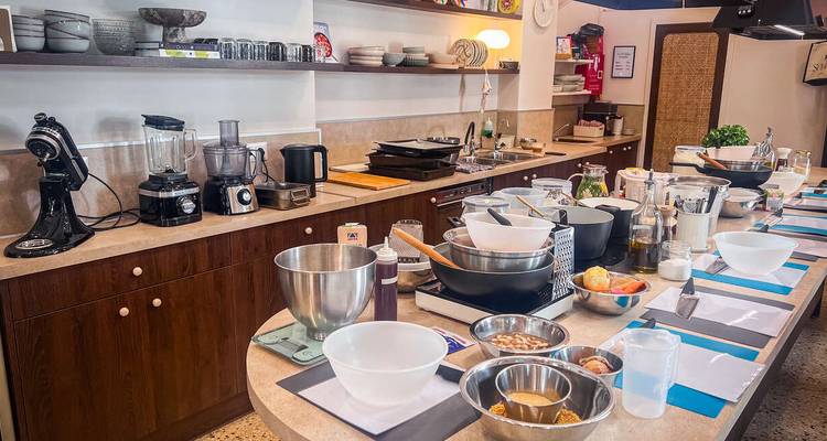 Cocina de enseñanza moderna equipada para una clase de cocina con batidoras, tazones e ingredientes ordenadamente dispuestos en cada estación de trabajo.