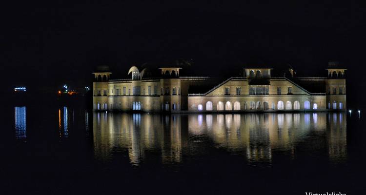 Jal Mahal palace reflected in water at night.