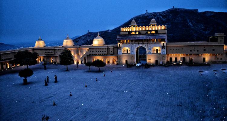 A fort illuminated at night with a mountainous backdrop.