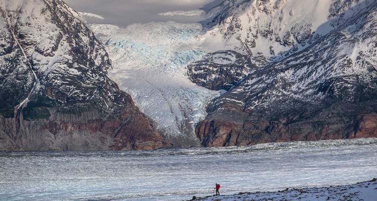 Een kleine figuur tegen een uitgestrekte gletsjer in een ruig berglandschap.