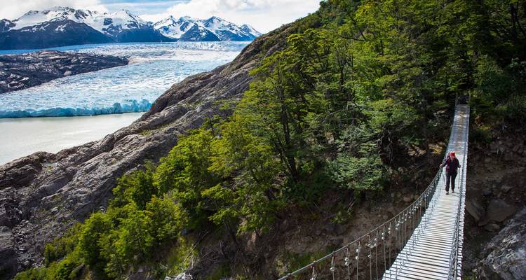 Wandelaars die een hangbrug oversteken met uitzicht op een gletsjer.