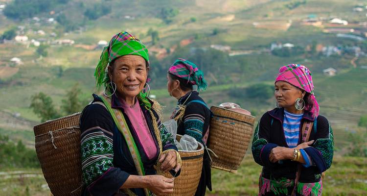 Trois femmes en tenue traditionnelle avec des paniers sur une colline.