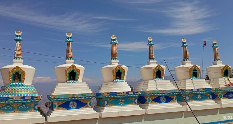 Colorful stupas under a blue sky with mountains in the distance.