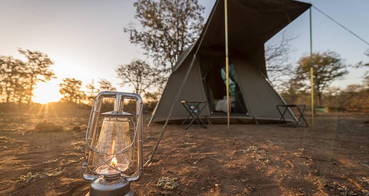 Tent campsite at sunset with a lit lantern in the foreground.