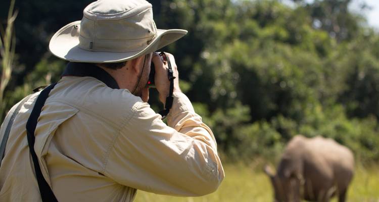 Person photographing a rhinoceros in the wild.