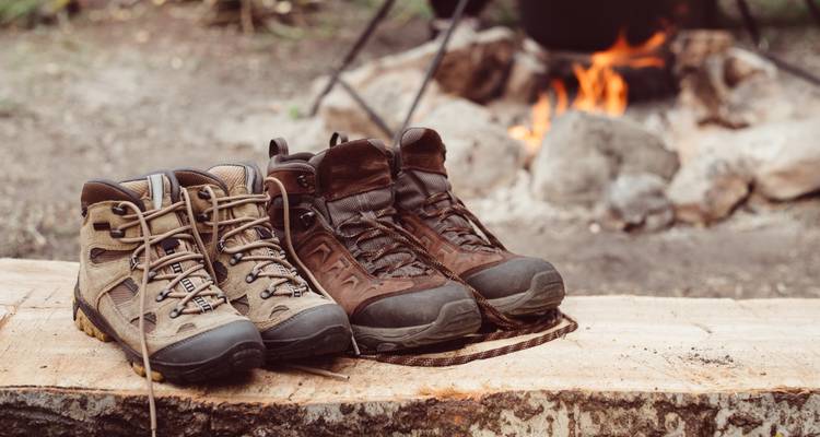 Four hiking boots on a wooden surface with campfire in the background.
