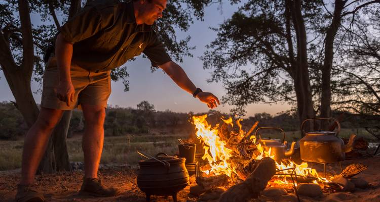 Man tending to a campfire with sunset in the background.