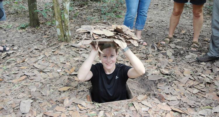 Visitante emergiendo de una trampilla de camuflaje estrecha en el suelo del bosque en el sitio de los túneles de Cu Chi.