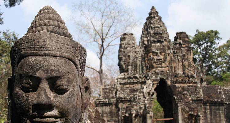 Escultura de rostro de piedra antigua cerca de una puerta ornamentada de templo ubicada en un entorno de selva.