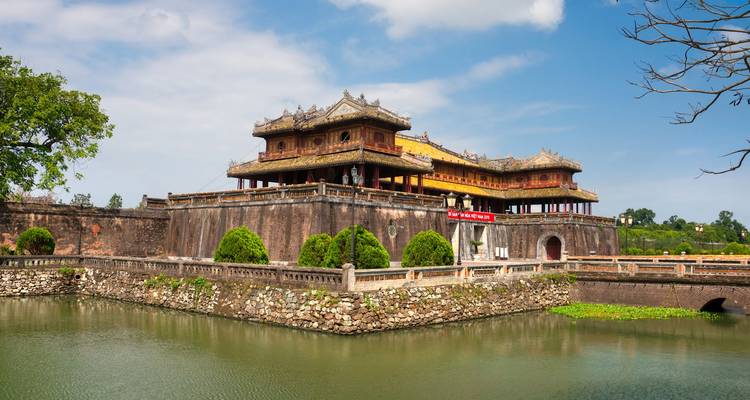 Le Palais Thai Hoa de la Citadelle de Hue, forteresse entourée de douves ressemblant à une forteresse, s'élève au-dessus d'une eau verte immobile et de ponts de pierre ornés sous des cieux bleus.