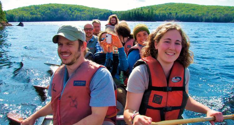 Grupo de personas navegando en canoa en un lago con colinas boscosas al fondo.
