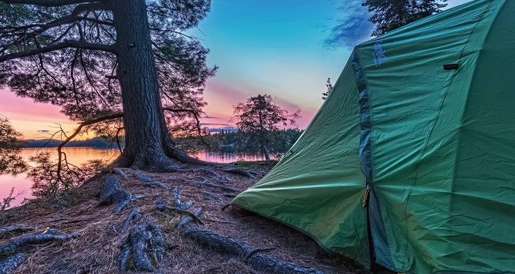 Tienda de campaña junto a un lago con un cielo colorido de atardecer.