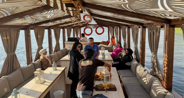 Interieur van een overdekte riverboat met gevoerde zitplaatsen waar een kleine groep gezellig wat eet en drinkt.