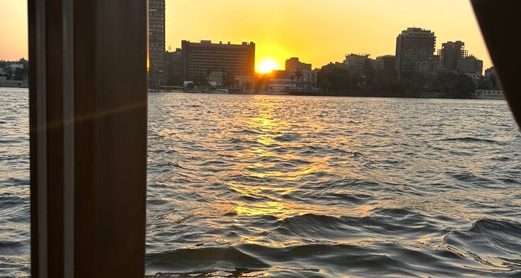 Gouden zonsondergang boven een brede rivier met silhouetten van de stadsskyline en rimpelend water op de voorgrond.