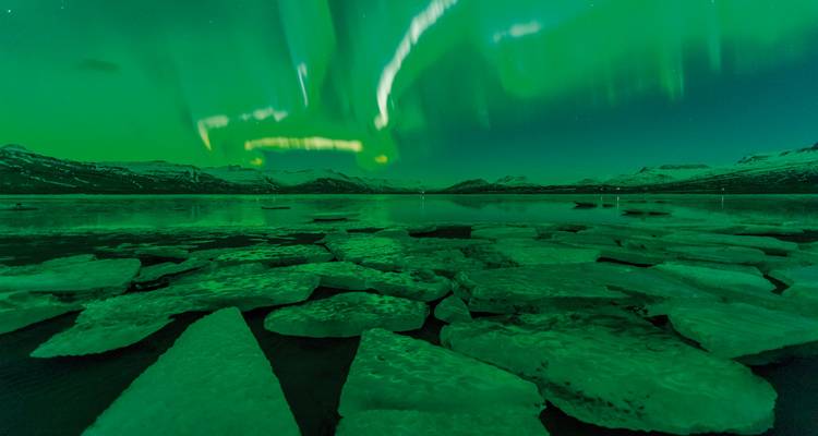 Auroras boreales vívidas sobre un lago helado con icebergs flotantes.