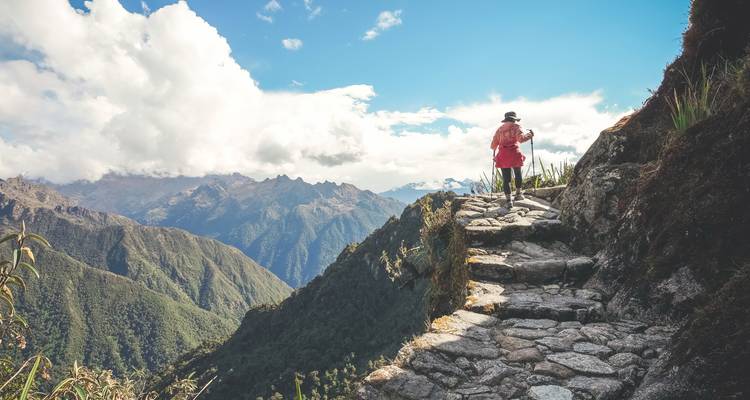 Een persoon die langs een stenen pad loopt in een bergachtig landschap.