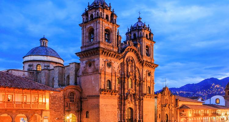 La cathédrale illuminée de Cusco brille contre un ciel crépusculaire d'un bleu vibrant avec les sommets andins au-delà.