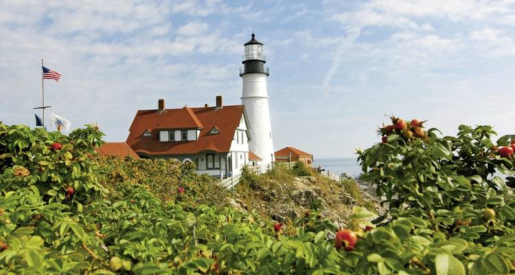 A lighthouse on a rocky coastline with an American flag nearby.